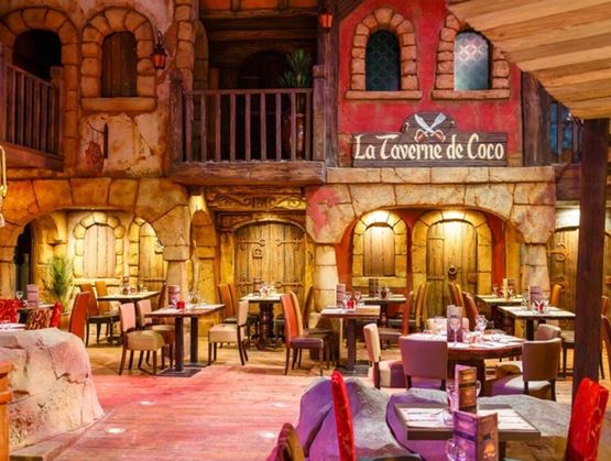 Une salle de restaurant thématisée rappelant une taverne chaleureuse, avec des tables dressées, une décoration en pierre et bois, et une ambiance conviviale et immersive.