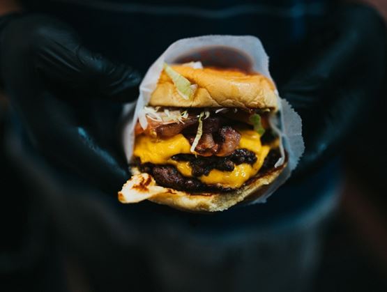 Close-up of a cheeseburger with bacon held by gloved hands