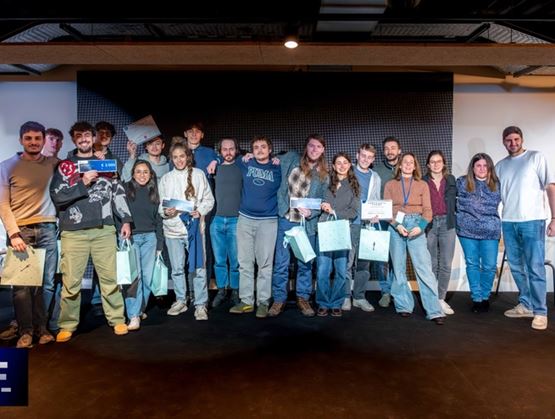 Group photo on stage at an event, with participants holding certificates and gift bags.