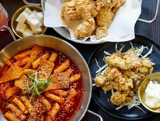 Spicy tteokbokki (rice cakes) sprinkled with sesame, served with fried chicken and small bowls of sauces and pickled radish.