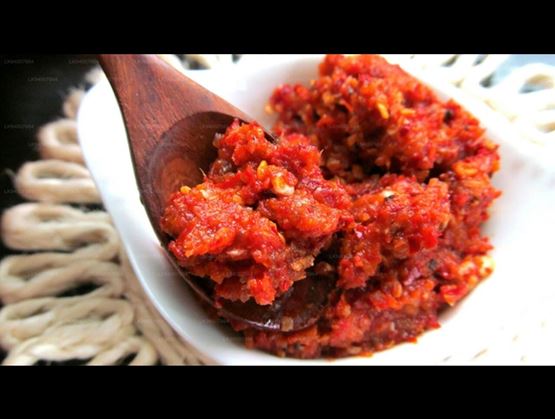 Spicy red chili paste in a white bowl with a wooden spoon.