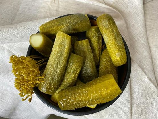 Whole pickles arranged on a black plate, with a sprig of dill.