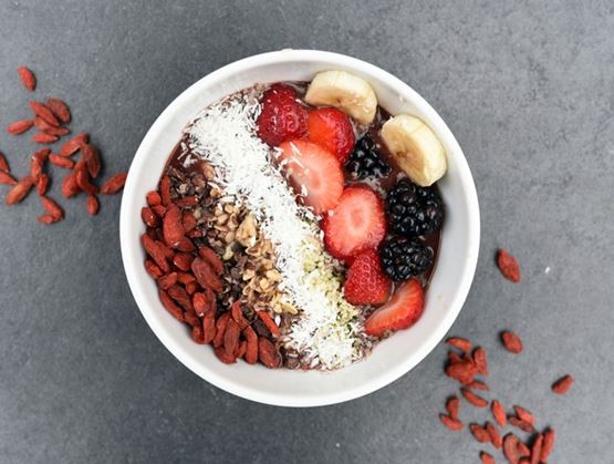 Smoothie (acai-style) bowl topped with strawberries, blackberries, banana, nuts, shredded coconut and goji berries.