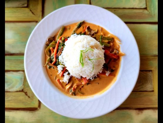 Plate of white rice in the center, surrounded by a creamy vegetable curry, on a wooden table.