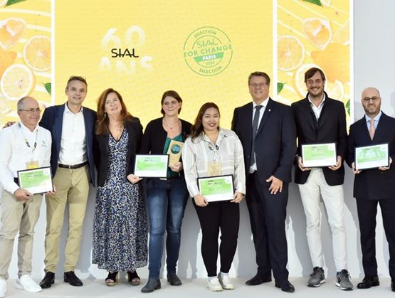 Group of award winners posing on stage at the SIAL For Change selection, holding certificates in front of a yellow citrus-themed backdrop.