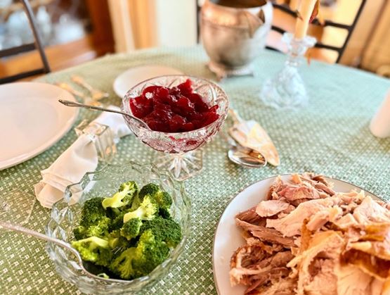 Set dining table with dishes including broccoli, sliced meat, and a red compote served in glass bowls.