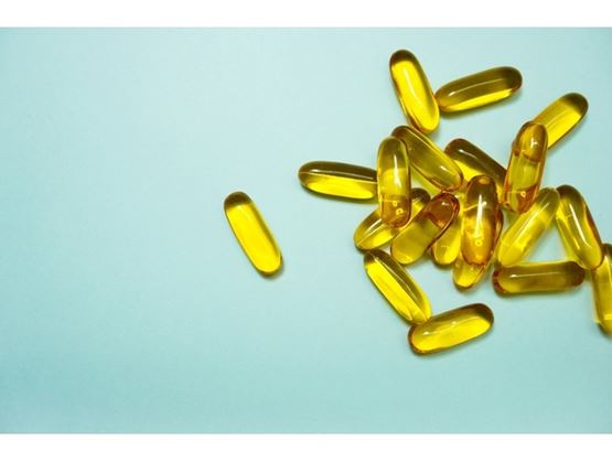 Des capsules jaunes translucides, probablement des compléments alimentaires, sont disposées sur un fond bleu clair.
