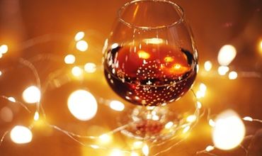 Verre de cognac ambré posé sur une surface, entouré de guirlandes lumineuses dorées créant une ambiance chaleureuse et festive avec un effet de bokeh en arrière-plan.