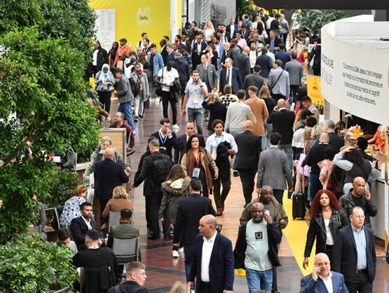 Crowded aisle at a trade show with many visitors and exhibitors moving between stands in a busy indoor exhibition space.