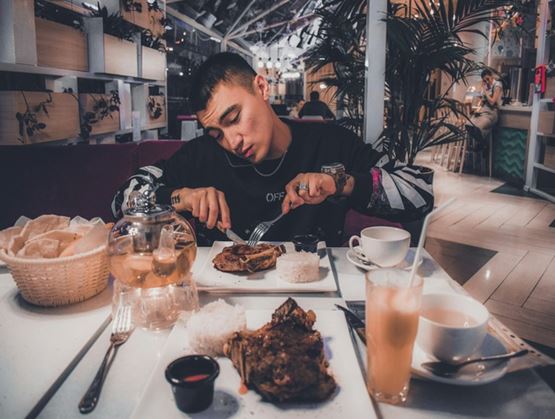 Un homme mange un plat de viande dans un restaurant, assis à table avec des boissons et un service de table complet dans une ambiance moderne.