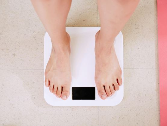 Person’s feet standing on a white digital bathroom scale on a tiled floor, with a pink yoga mat nearby.