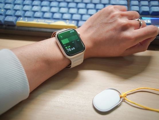 Personne portant une montre connectée affichant la fréquence cardiaque sur son poignet, posée sur un bureau devant un clavier d’ordinateur.
