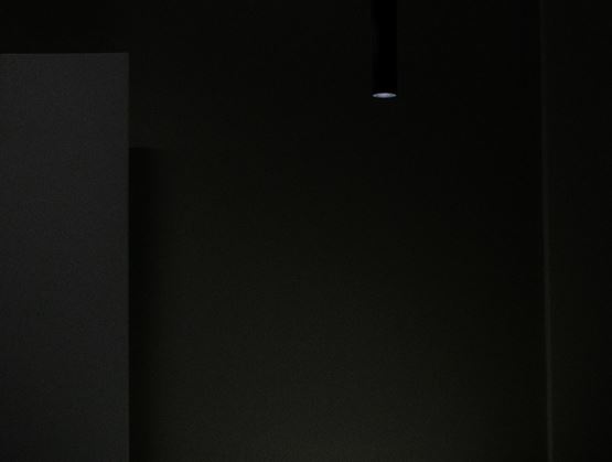 A minimalist table lit by two pendant lights in a dark setting, with a plated dish and a glass of wine creating an intimate atmosphere.