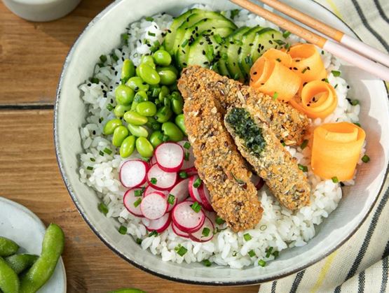 Bol de riz garni de légumes frais, d’edamame, de radis, d’avocat et de sticks panés, servi avec des baguettes et de la sauce soja.