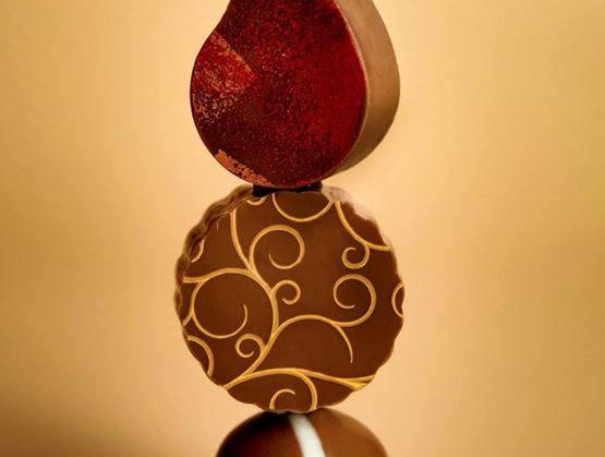 Il s'agit d'une élégante pile de chocolats magnifiquement confectionnés, aux motifs raffinés, surmontée d'un chocolat rouge brillant. On dirait une délicieuse œuvre d'art !