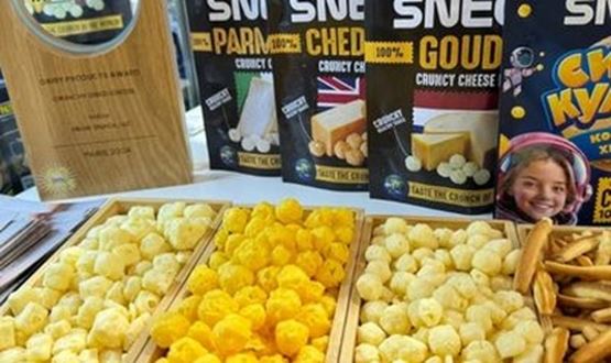 Display of innovative cheese snacks at a trade show booth, with various crunchy products presented in trays and their packaging visible in the background.