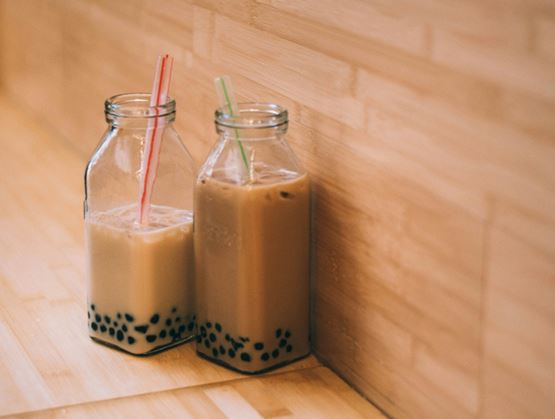 Deux bouteilles en verre remplies de thé au lait avec perles de tapioca, chacune munie d’une paille, posées sur une surface en bois dans une ambiance chaleureuse.