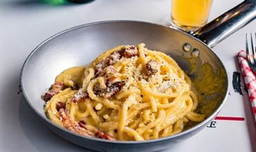 Carbonara pasta served in a pan with grated cheese and black pepper.
