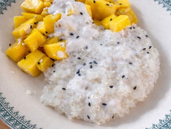 Assiette de riz gluant crémeux accompagnée de morceaux de mangue, nappée de lait de coco et parsemée de graines de sésame.