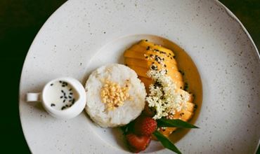 Assiette dressée avec du riz moulé, des tranches de mangue, des fraises, une sauce crémeuse et des graines, présentée de manière élégante.