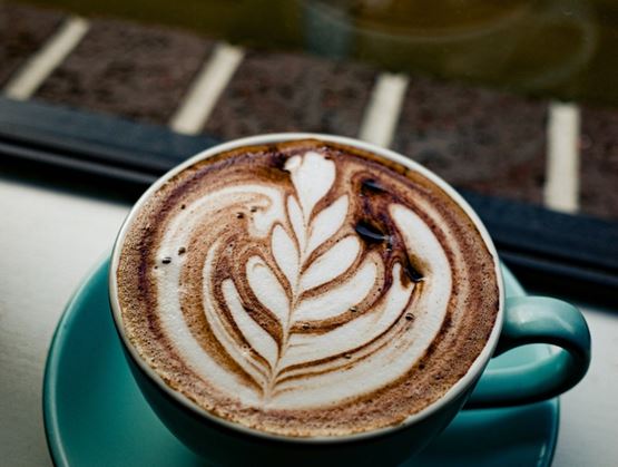 Voici une tasse de café magnifiquement préparée, ornée d'un motif de latte art très raffiné. Les volutes et les motifs en forme de feuilles apportent une touche artistique à ce café riche et onctueux.