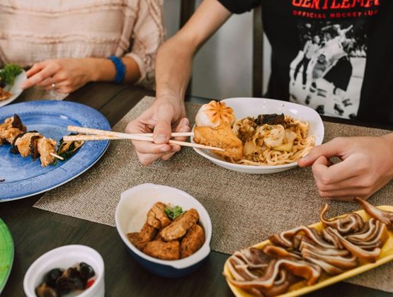 Repas partagé autour d’une table avec plusieurs plats asiatiques, dont des nouilles, des bouchées vapeur et des brochettes.