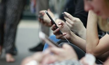 Seated people using their smartphones, with a close-up of a hand holding a phone.