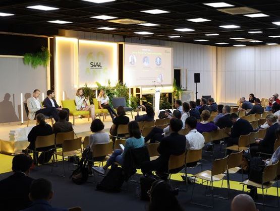 Conférence professionnelle avec un panel d’intervenants sur scène devant un public assis, dans un espace événementiel moderne.