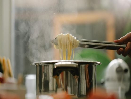 Spaghetti being lifted with tongs above a steaming pot.