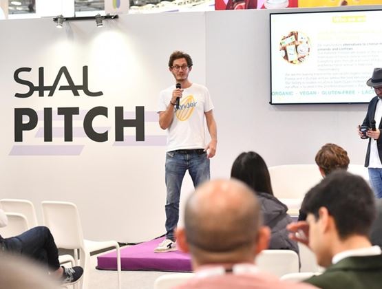 SIAL Pitch presentation with a speaker holding a microphone in front of an audience at a trade show.