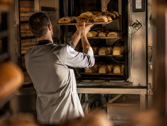 Boulanger plaçant un plateau de pains tout juste cuits dans un four professionnel.