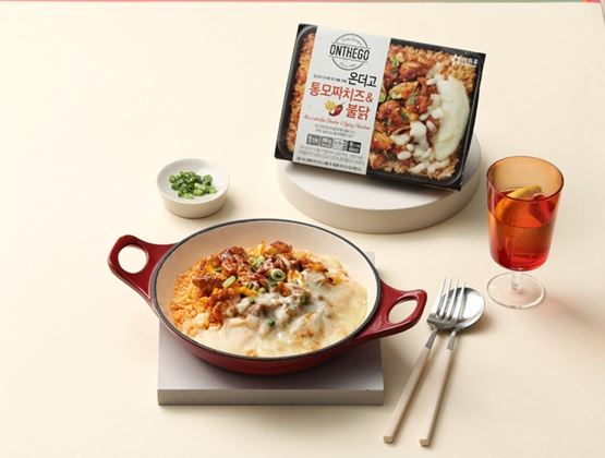 Plat gratiné dans une casserole rouge, accompagné d’un emballage de repas préparé, d’un verre et de couverts.