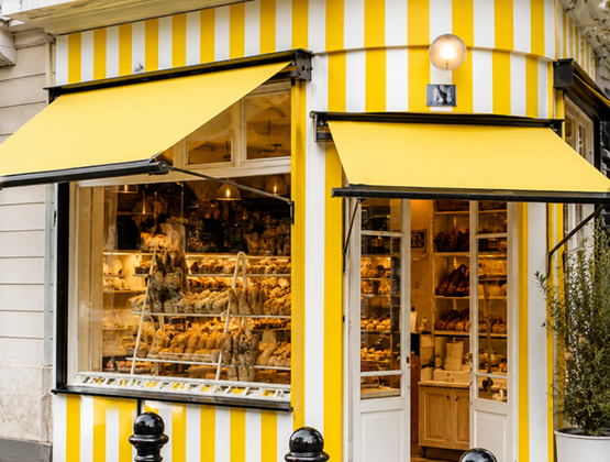 Bakery storefront with yellow and white stripes, featuring display windows filled with breads and pastries.
