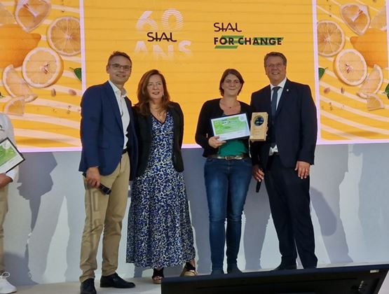 Quatre personnes posent sur scène lors d’une remise de prix SIAL for Change, avec une lauréate tenant un certificat et un trophée.
