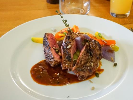 Assiette gastronomique avec morceaux de viande grillée, sauce brune et légumes colorés.