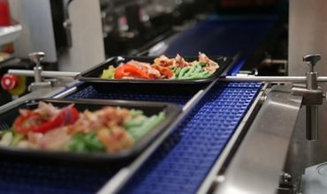 Barquettes de repas préparés avec légumes et viande sur une ligne de production alimentaire.