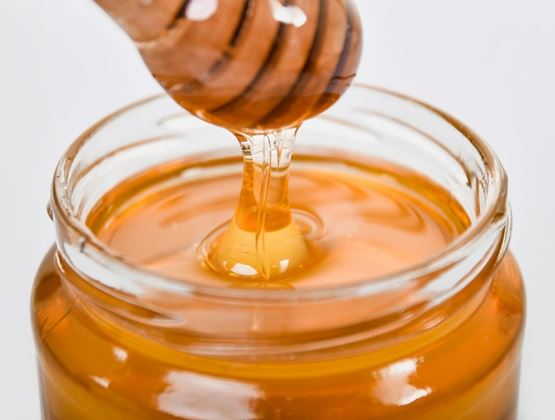 Golden honey dripping from a wooden dipper into a glass jar.