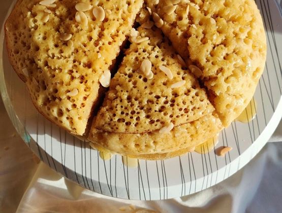 Crêpe épaisse découpée en parts, garnie d’amandes effilées et de miel sur une assiette.