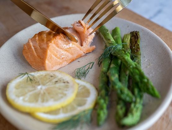 Salmon fillet served with grilled asparagus, lemon slices and dill on a plate.