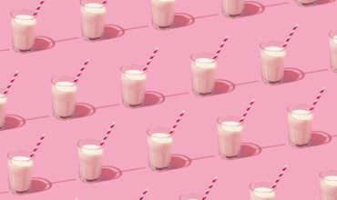 Repeating pattern of glasses of milk with red and white striped straws, arranged on a pink background.