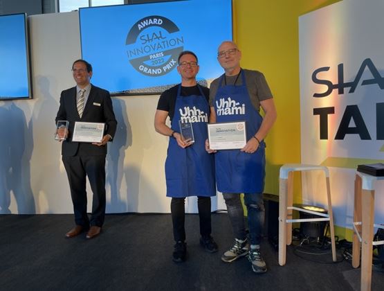 Trois hommes sur scène lors de la remise du Grand Prix SIAL Innovation 2022, tenant des trophées et certificats, avec deux participants portant des tabliers Uhhmami.