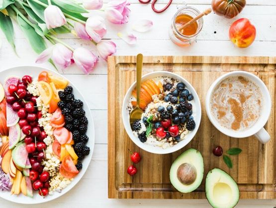 Colourful healthy breakfast spread with fresh fruit, berries, avocado, smoothie bowl, honey and coffee on a bright table.