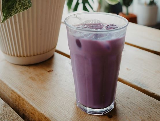 Glass of iced purple drink on a wooden table, next to a potted green plant.
