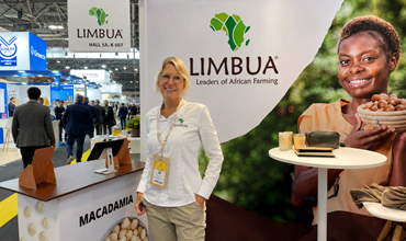 LIMBUA representative standing at the company’s macadamia stand during a trade show, with branded signage and exhibition booths in the background.