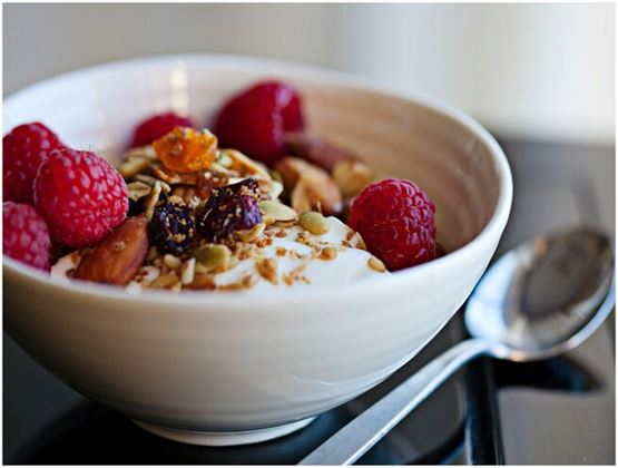 Bol de yaourt ou dessert végétal garni de framboises, granola, graines et fruits secs, avec une cuillère à côté.