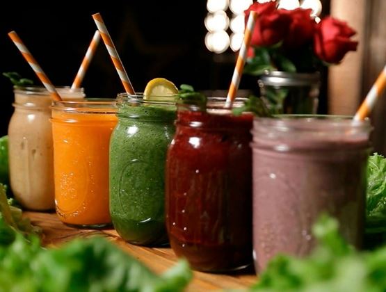 Jars of colorful smoothies with striped straws, arranged on a wooden table among lettuce leaves.