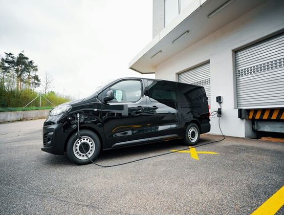 Véhicule utilitaire électrique en recharge devant un entrepôt logistique, illustrant le transport urbain à faibles émissions.