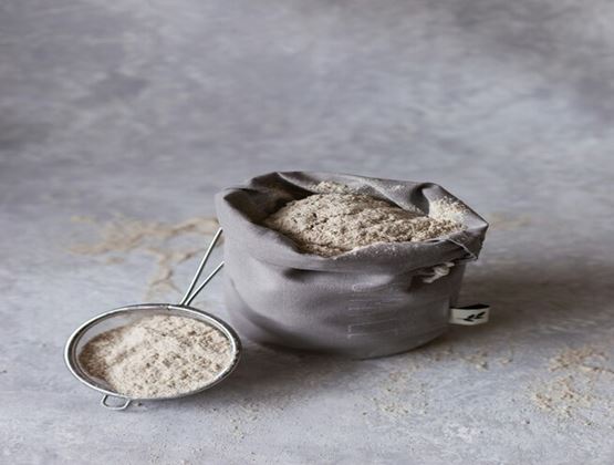 Bag of flour with a small sieve on a grey surface, illustrating baking ingredients and food preparation.
