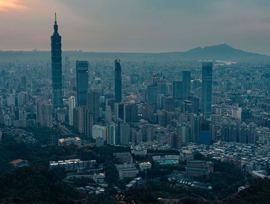 Panoramic view of Taipei skyline at dusk, with Taipei 101 rising above the city and mountains in the background.