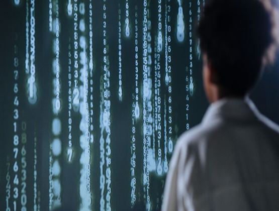 Personne observant un écran affichant des lignes de chiffres lumineux, évoquant la cybersécurité et la surveillance des données.